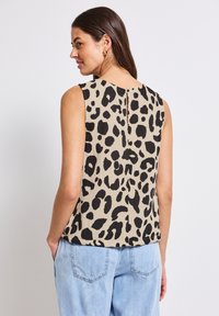 Top sans manches beige avec imprimé léopard noir. Présente une fente dans le dos et une coupe décontractée, associé à un jean bleu clair.