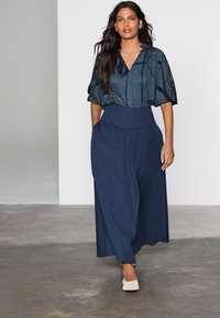 Navyblå vidde bukser med høj talje, kombineret med en kortærmet, mørk mønstret bluse med V-hals. Teksturerede stoffer detaljer.