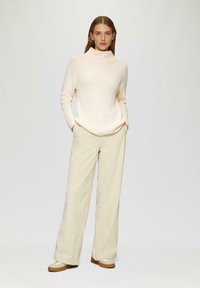 Lichtbeige geribde coltrui met lange mouwen, gecombineerd met crème wijde broek en beige schoenen met witte accenten.