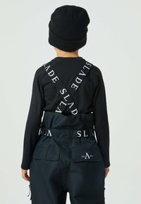 Svart långärmad tröja med ribbade detaljer, kombinerad med mörkblå arbetsbyxor med justerbara axelband och logotypdetalj. Fickor på baksidan.