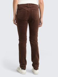 Pantalones de pana marrón de corte slim, con dos bolsillos traseros y una cinturilla. Lleva puestos unas zapatillas blancas. La textura es suave y acanalada.