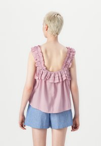 Mouwloos roze top met gerimpelde schouderbanden en een detail aan de achterkant, gecombineerd met blauwe gestreepte shorts. Glad stof, licht en luchtig ontwerp.