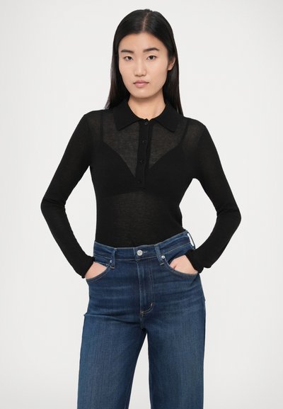 Črna, dolgorokavna majica z ovratnikom in zapiranjem na gumbe, izdelana iz prosojnega materiala. Kombinirana z visokim pasom modrih kavbojk.