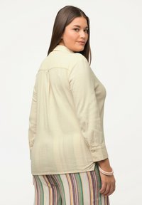 Cremefarvet langærmet skjorte med button-down krave, tekstureret stof og bageste plissering, parret med flerfarvede stribede bukser.