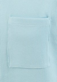 Tejido de punto azul claro con un bolsillo cuadrado de parche que presenta un patrón texturizado y acanalado.