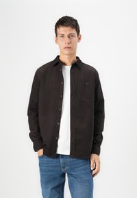 Zwarte button-up shirt van katoen, met een borstzak, lange mouwen en een klassieke kraag, gelaagd over een wit t-shirt.