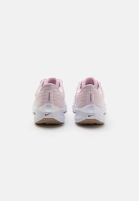 Par de zapatillas deportivas de color rosa claro con suelas blancas, vistas desde la parte trasera, con tiras reflectantes en el talón y pequeños logotipos negros de Nike.