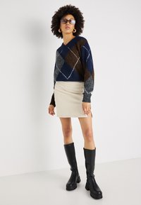 Sweter w serek w kolorze granatowym, brązowym i szarym z diamentowym wzorem; zestawiony z kremową spódnicą z kordurowej tkaniny i czarnymi wysokimi butami na platformie.