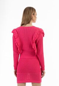 Fuchsia stickad klänning med volanger vid ärmarna, strukturerat mönster, ribbad midja och nederkant, med öppet stickade detaljer och en figurnära silhuett.