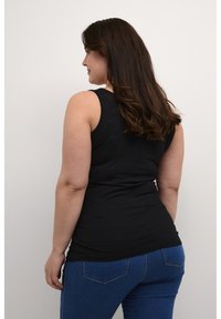 Top negro sin mangas con una silueta ajustada, combinado con jeans de denim azul que tienen bolsillos traseros y una textura suave.