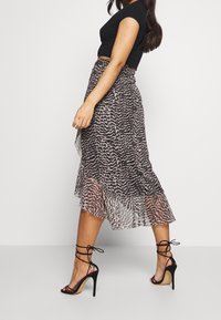 Top corto nero abbinato a una gonna midi fluida e trasparente con motivo animalier leopardato in tonalità scure e chiare, e tacchi neri con cinturini.
