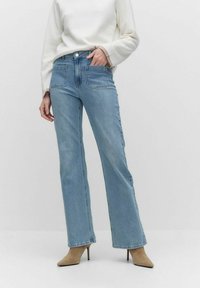 Ljust blå denimjeans med hög midja, vida ben och två framfickor. Bärs med en krämfärgad tröja och beiga klackskor.