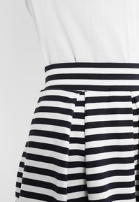 Gonna a righe con strisce orizzontali blu navy e bianche, design plissettato e cintura blu navy unita. Realizzata in un tessuto testurizzato.