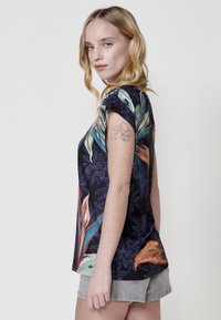 Haut à manches courtes à motifs floraux avec une base bleu marine foncé, des motifs de feuilles vibrants en vert, orange et bleu, et un design ample.