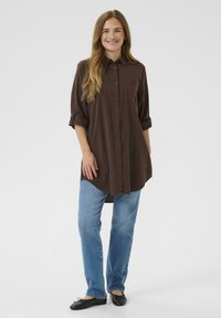 Barna zsebes gombos ing, feltűrt ujjakkal, világoskék egyenes szárú farmerrel és fekete balerinacipővel párosítva. Egyszerű, kényelmes szabás.