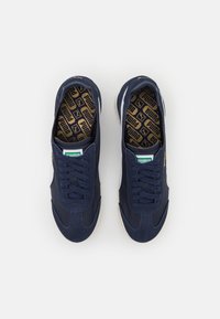 Zapatillas azul marino con parte superior de ante y malla, detalles en blanco, cordones planos y una plantilla con un patrón que presenta un logotipo de la marca.