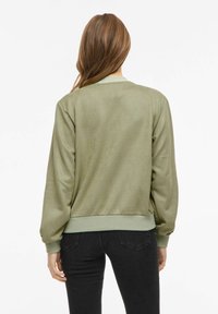 Zielona kurtka bombowiec o miękkiej, gładkiej fakturze, ze ściągaczami na mankietach i u dołu oraz luźnym krojem. Posiada prosty design bez wzorów.