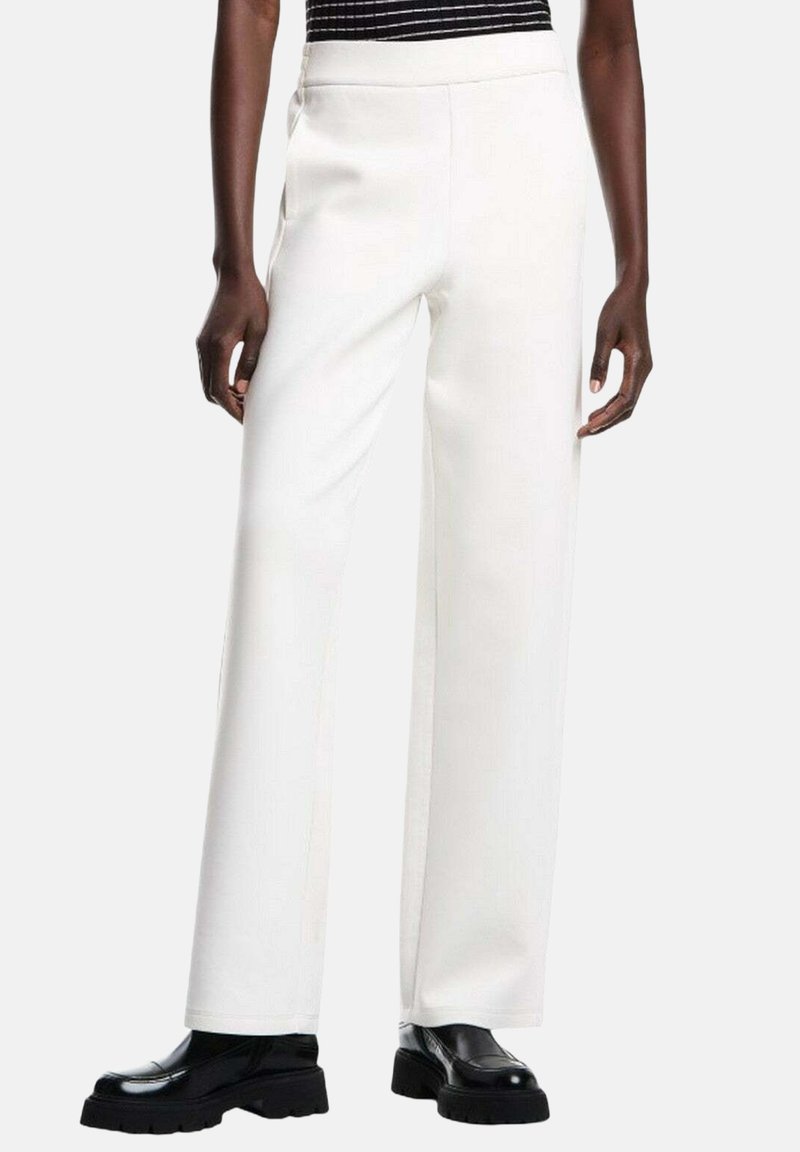 Pantaloni bianchi a gamba larga realizzati in tessuto morbido con una cintura elastica, abbinati a scarpe nere chunky per un contrasto audace.