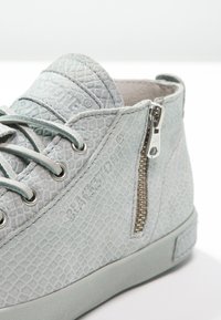 Světle modré texturované vysoké tenisky s hadím vzorem, vybavené bočním zipem a kulatými kovovými očky na tkaničky.