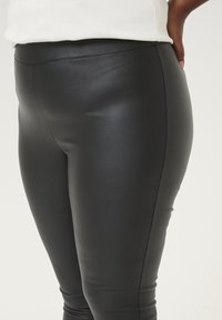 Schwarze Kunstlederleggings mit einer glatten, glänzenden Textur, ausgestattet mit einem hohen Bund und einer engen Passform entlang der Beine.