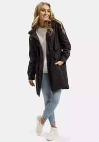 Czarna kurtka do pasa z wciśniętą talią, kapturem i kieszeniami z przodu. Noszona na białą bluzkę i niebieskie dżinsy z białymi trampkami.