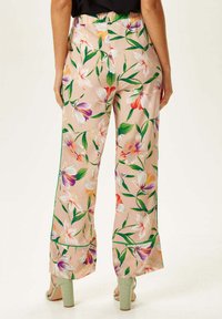 Floral print trousers in light peach with green accents. Features large pink and purple flowers, wide legs, and a relaxed fit.