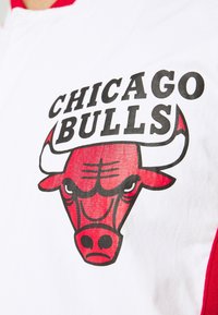 Hvid T-shirt med et stort rødt og sort Chicago Bulls-logo, der viser et bulls hoved og tekst ovenfor, detaljeret med fed skrift og accenter.