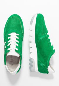 Sneaker verde in suede con lacci e dettagli bianchi. Presentano una tomaia perforata, una robusta suola in gomma bianca e un design a punta arrotondata.