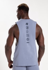 Lichtgrijze mouwloze tanktop met een klassieke pasvorm, voorzien van bedrukte graphics en logo's op de achterkant. Zachte stof en een relaxte uitstraling.