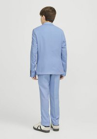 Costume bleu clair avec une veste à un bouton et un pantalon assorti. Tissu lisse, coupe ajustée, associé à des baskets décontractées.