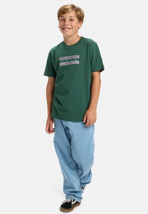 Groene katoenen t-shirt met een graphic print en korte mouwen, gecombineerd met lichtblauwe denim broeken en zwarte sneakers.