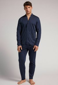 Conjunto de pijama azul marino que incluye una camisa de botones de manga larga con cuello tipo banda y pantalones ajustados. Fabricado con un tejido ligero y suave.