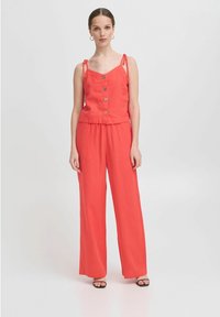 Koralli värvi jumpsuit reguleeritavate nööridega, nööpidega ees ja laia säärega püksid. Valmistatud kergest kangast, pakkudes vabamat istuvust.
