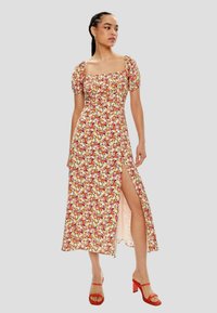 Vestido maxi floral con escote cuadrado, mangas abullonadas y una abertura alta en el muslo. La tela tiene un patrón de flores coloridas sobre un fondo claro.