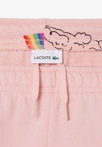 Los pantalones de chándal de algodón rosa de Lacoste presentan una cintura con cordón, una etiqueta de arcoíris y un bordado de nubes cerca de la cinturilla. Textura suave en toda la prenda.