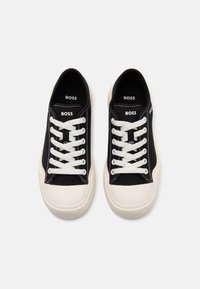 Črne teniske iz platna z belimi vezalkami, ki imajo kontrastno off-white gumijasto podplat in logo "BOSS" na jezičku.