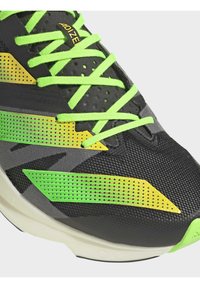 Gros plan sur une chaussure de course noire et grise avec des lacets vert fluo et des accents de design à pois jaune-vert sur le côté et l'avant.