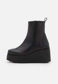 Bottines en cuir noir avec une semelle en coin, texture lisse, bout rond, haute plateforme et une boucle à l'arrière pour un enfilage facile.