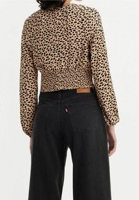 Cropped blouse met luipaardprint in tan en zwart, met een smock taille en lange mouwen. Gecombineerd met hoge zwarte spijkerbroeken.