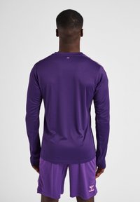 Langærmet atletisk skjorte i lilla med en glat tekstur og minimalt design. Har en rund halsudskæring og lyserød logo detalje på shorts.