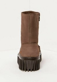 Bottine en cuir suédé marron mi-mollet avec une épaisse semelle à plateforme noire nervurée et une fermeture éclair sur le côté, présentée de dos sur un fond blanc.