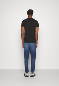 Camiseta negra de manga corta combinada con vaqueros azules ajustados y zapatillas negras con detalles blancos. Vista desde atrás.