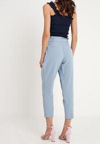 Světle modré kalhoty na míru se zúženým střihem, se stranovými a zadními kapsami, doplněné světlým růžovým sandálem na blokovém podpatku.