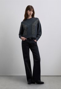 Maglione corto grigio scuro con coste testurizzate e decorazioni, abbinato a jeans neri a gamba larga e vita alta e scarpe nere.