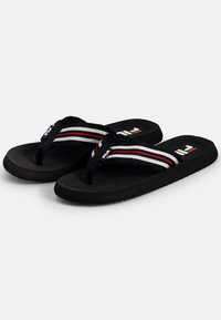 Mustat flip-flopit, joissa on teksturoitu pohja ja kudotut hihnat mustana, valkoisena ja punaisena. Fila-logo pohjassa ja hihnoissa.