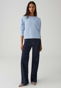 Maglione a righe azzurro chiaro e bianco con maniche a tre quarti, abbinato a jeans a gamba larga blu scuro e scarpe beige con punta appuntita.