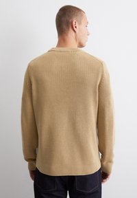 Beige gerippter Pullover mit langen Ärmeln und Rundhalsausschnitt, mit einem strukturierten Strickmuster und einem gesäumten Saum am unteren Ende.