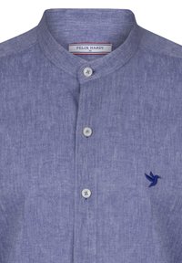 Camisa de lino azul claro con cuello alto, que cuenta con tres botones y un pequeño logo de colibrí bordado en azul oscuro.