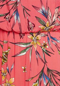 Koraalroze stof met een bloemmotief met gele, witte en roze bloemen, groene en blauwe bladeren en gedetailleerde plooien.