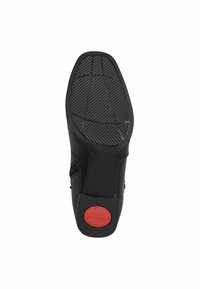 Suela de zapato negra con una superficie de goma texturizada y un acento circular rojo marcado como "Confort". Presenta patrones de rejilla para una mejor tracción.